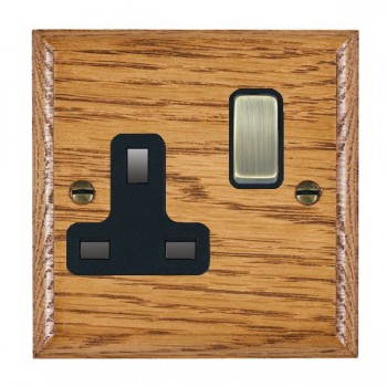 Hamilton Woods Ovolo Medium Oak 1 Gang 13A Double Pole Switched Socket with Antique Brass Rocker and Black Surround